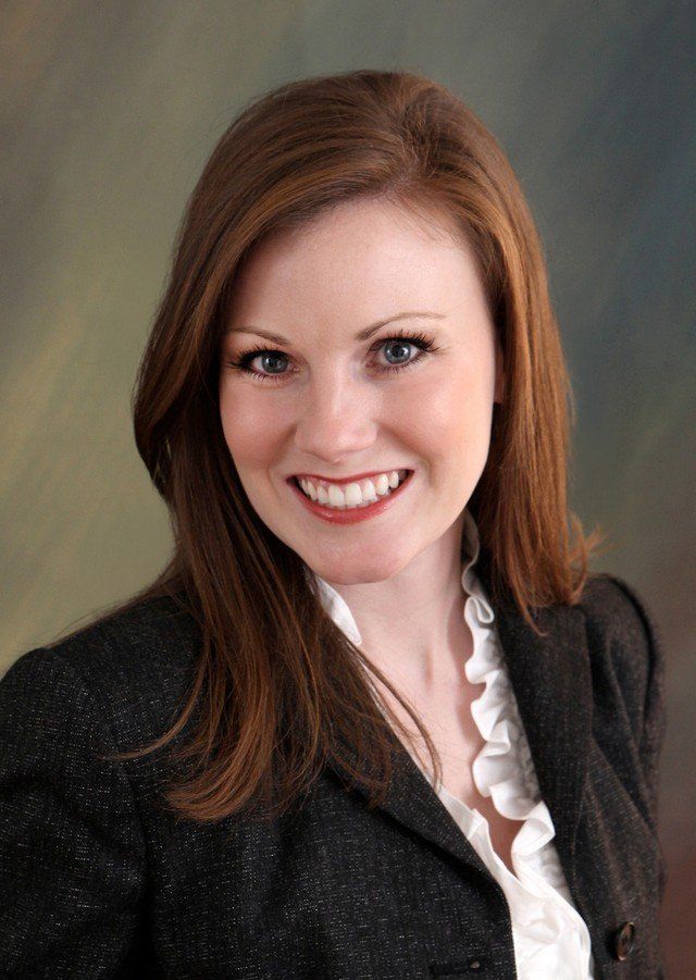 A woman with red hair is wearing a black jacket and smiling